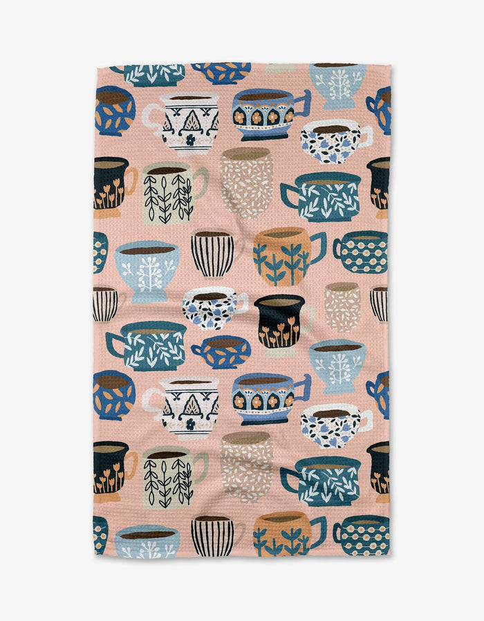 Les Tasses by Cottonflower Studio is an ultra-absorbent Geoweave™ cloth featuring rows of illustrated mugs and cups in blue, black, white, and tan on a light pink background with decorative patterns.