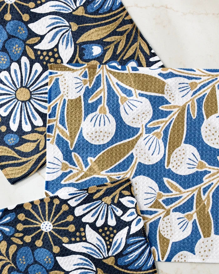 The Amy MacCready Leslie Flowers set includes three recycled dishcloths featuring unique floral, leaf, and berry patterns in blue, white, gold, and black on a light marble background.