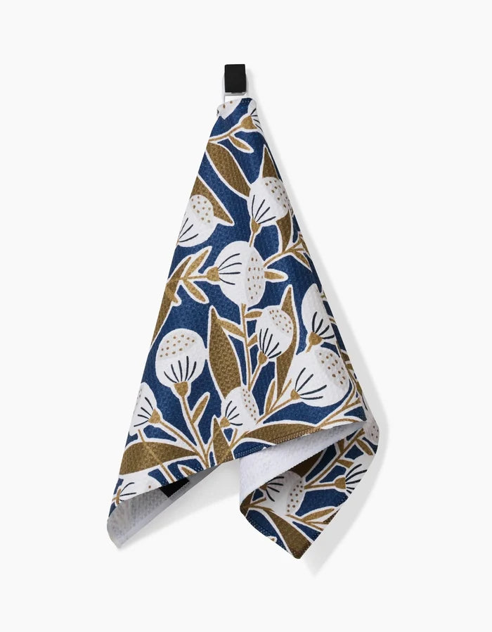 The Leslie kitchen towel by Amy MacCready features ultra-absorbent Geoweave fabric with a white and brown floral pattern on a dark blue background, shown hanging against a plain white surface.