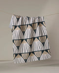 The Letitia recycled kitchen towel by Amy MacCready features rows of stylized fan or shell shapes in a geometric pattern with black, white, and tan semicircles, and hangs from a string against a neutral background.