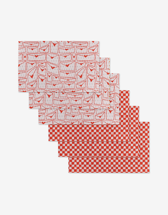 Six rectangular Letters of Love placemats by Kayla Ann—three with a red and white envelope design, three with a red and white checkered pattern—are stacked neatly, crafted from post-consumer recycled materials.