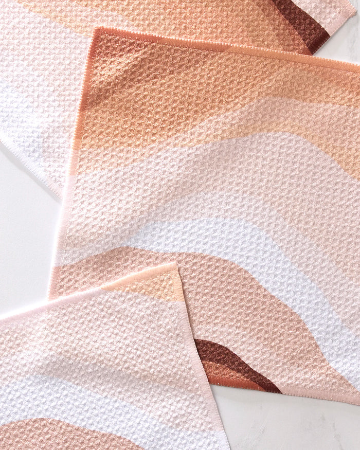 The Levels of Fall dishcloth set by GEOMETRY features three eco-friendly, recycled dishcloths with wavy abstract patterns in peach, tan, brown, and white, partially overlapping on a light surface.