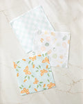 Three super-absorbent “Life is Beautiful” dishtowels by Sweet Simple Vegan are displayed on a marble surface: one with a blue gingham pattern, one with orange and green vegetable doodles, and another with an orange butterfly and floral design.