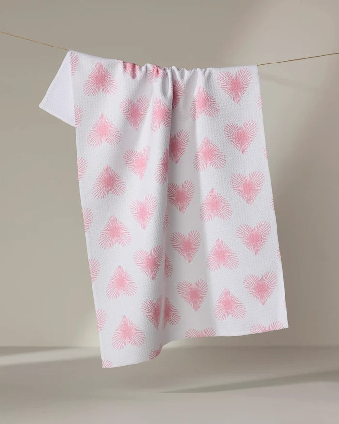 The Hufton Studio Life Line Hearts towel, featuring pink heart patterns on a quick-drying white fabric, is draped over a clothesline against a neutral background.