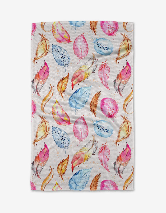 The Light as a Feather kitchen towel by Elena Fay is white, made from recycled materials, and features a random pattern of watercolor-style feathers in pink, blue, orange, and yellow.