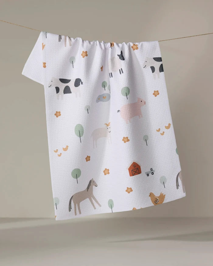 The Coit Creative "Light Farm Animals" tea towel, made from recycled materials and featuring farm animal illustrations, hangs textured and white against a neutral background.