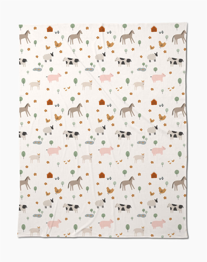 The Coit Creative Light Farm Animals blanket showcases a charming pattern of farm animals, trees, flowers, and barns on a white background. Made from eco-friendly recycled materials, its a cozy and conscious addition to your home.