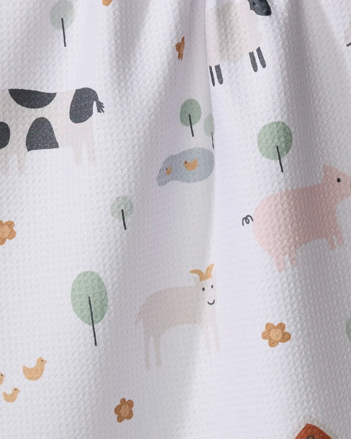 The Coit Creative Light Farm Animals kitchen towel features a white textured fabric adorned with pastel illustrations of cows, pigs, goats, sheep, chickens, trees, and yellow flowers. Made from recycled materials for an eco-friendly touch.