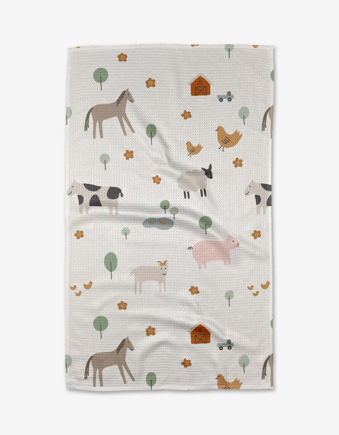 The Coit Creative Light Farm Animals tea towel is crafted from white Geoweave™ fabric and features a playful farm-themed pattern with illustrated animals, barns, trees, and small yellow flowers scattered across the surface.