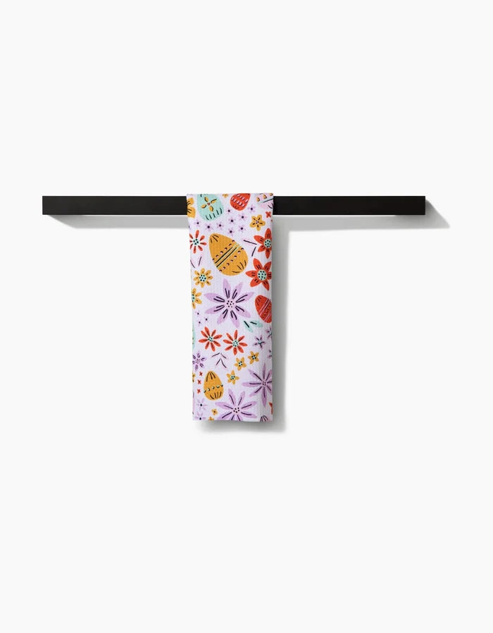 The Lilith towel by Amy MacCready, ultra-absorbent and white with vibrant floral and citrus prints, hangs neatly over a black rod against a plain white background.