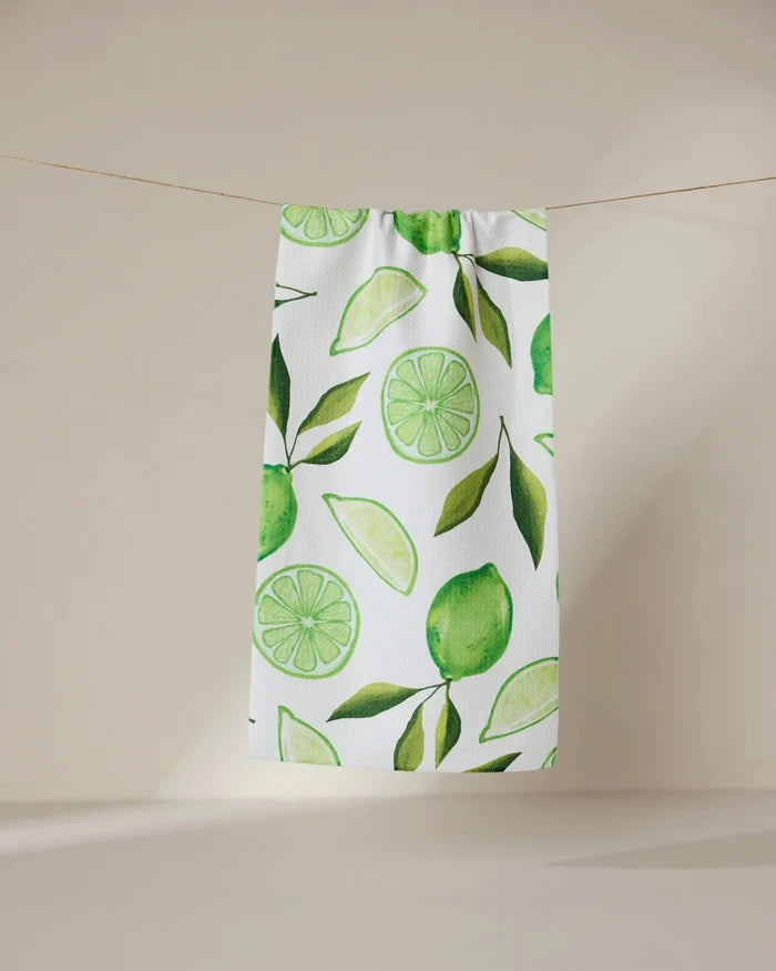 The GEOMETRY Lima kitchen towel, crafted from recycled materials and featuring green lime and leaf designs, hangs on a clothesline against a simple beige background.