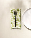 A silver fork rests on a GEOMETRY eco-friendly napkin featuring a limes pattern, set on a textured tablecloth beside a white plate partially visible to the right.