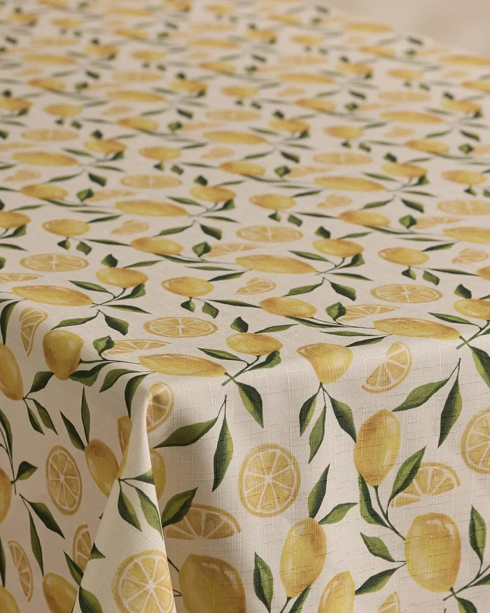 The Geometry Limoncello tablecloth has a cream background with a repeating pattern of whole lemons, lemon slices, and green leaves. Stain-resistant and stylish, its the perfect blend of function and flair for any dining space.
