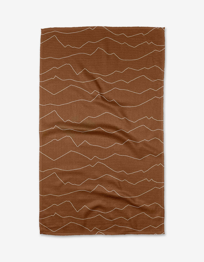 The Lined Mountains tea towel by Coit Creative features thin, wavy cream lines on brown Geoweave fabric, creating an abstract mountain-inspired design.
