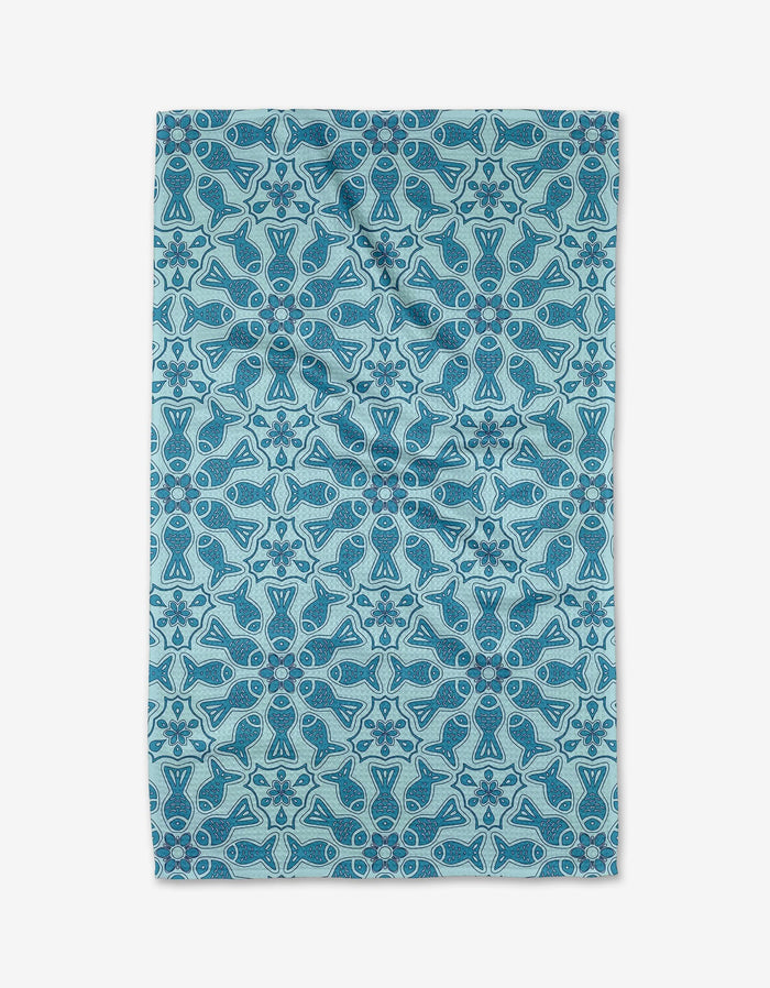 The Marta Harvey Little Fish Mandala tea towel features light blue Geoweave fabric with a symmetrical mandala of abstract fish and geometric shapes in darker blue and teal, arranged in rows and columns.