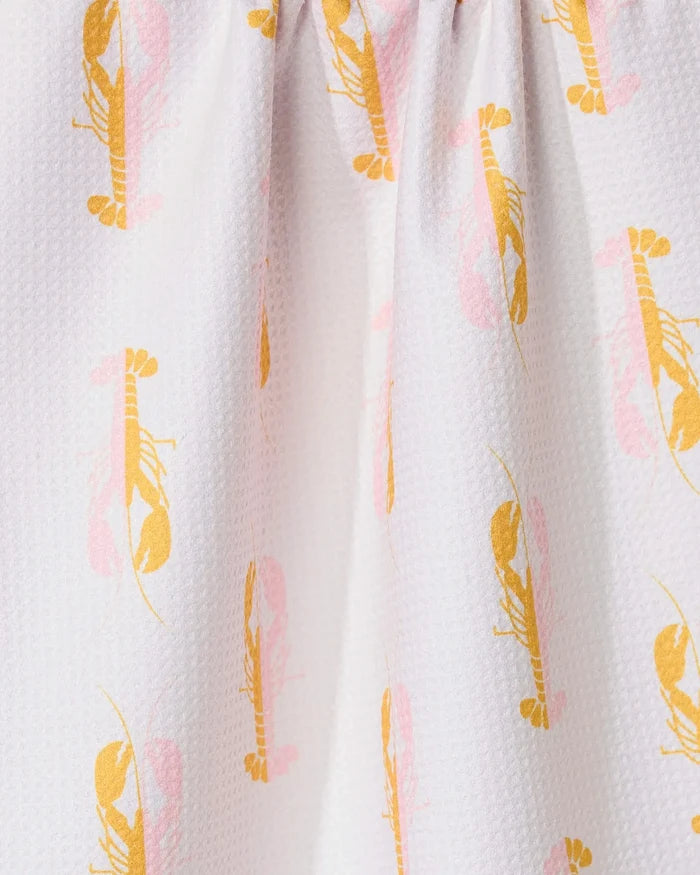 Close-up of GEOMETRYs Lobster Love kitchen towel, featuring a white textured fabric with an orange and pink lobster pattern. Made from recycled materials, the towel is gathered at the top to create gentle folds.
