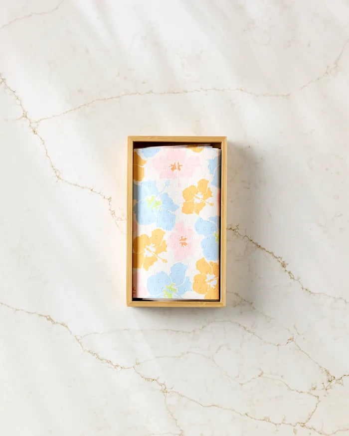 A rectangular wooden box from GEOMETRY holds "Lobster Love," a pastel floral eco-friendly cloth with blue, yellow, and pink flowers, displayed on a white marble surface streaked with light brown veins.