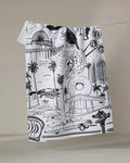 The Los Angeles kitchen towel by Elisabeth Wing is a white recycled towel with black line art, depicting iconic LA landmarks like the Hollywood sign, palm trees, a vintage car, donut shop, Ferris wheel, and street signs.