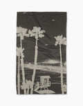 The Geometry Lost In Clemente blanket showcases a beige sketch of palm trees, a pier, and birds on a dark background, crafted from ultra-absorbent Geoweave fabric for comfort and style.