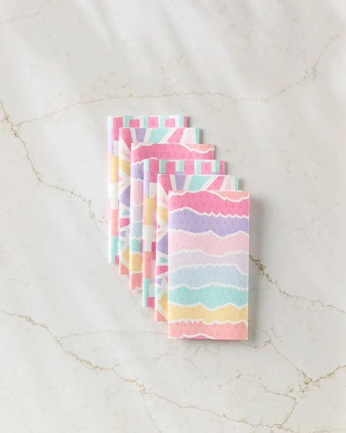 Six pastel-colored, reusable Lots of Dots paper towels by Rebecca Bobko are neatly stacked on a light marble surface.