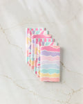 Six pastel-colored, reusable Lots of Dots paper towels by Rebecca Bobko are neatly stacked on a light marble surface.