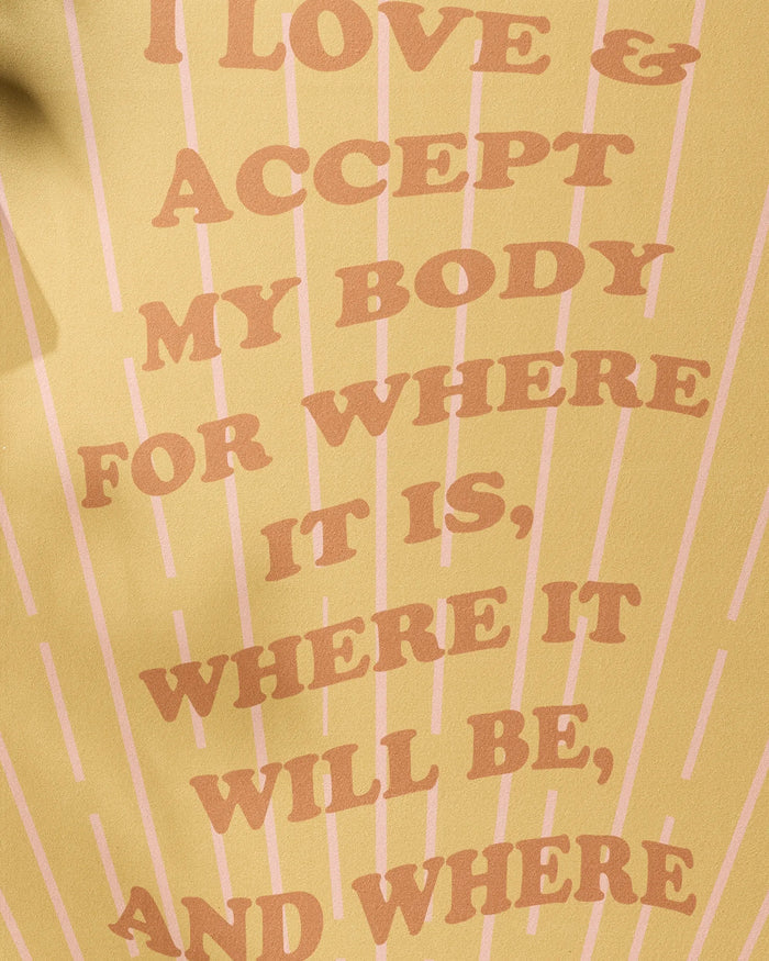 With a yellow background and pink lines, the "Love and Acceptance Affirmation" yoga towel by Arielle Estoria features bold text: I LOVE & ACCEPT MY BODY FOR WHERE IT IS, WHERE IT WILL BE, AND WHERE. Made from recycled materials to support self-love.