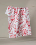The Love Birds kitchen towel by Hufton Studio, featuring a pink bird-on-branches pattern on white recycled fabric, hangs draped over a clothesline against a plain beige background.