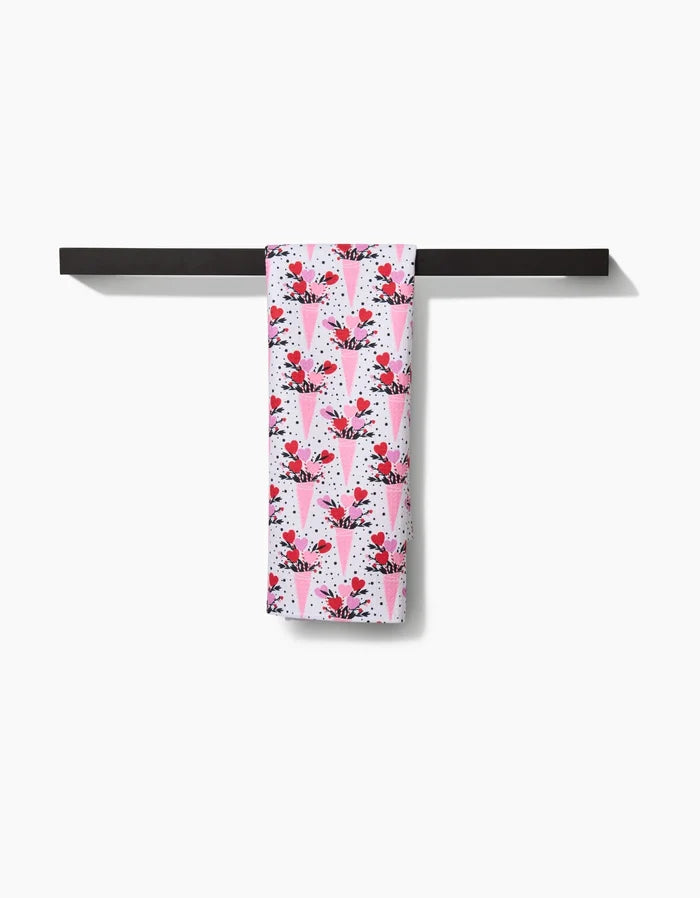 The Love Bouquet tea towel by Charlie Rowan Designs, featuring pink and white geometric berry and leaf patterns, hangs neatly on a horizontal black bar against a plain white background.