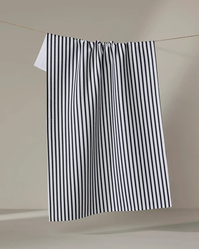 The Kailee Wright Love Notes kitchen towel, featuring black and white vertical stripes and quick-dry fabric, hangs neatly on a clothesline against a simple neutral background.