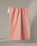 The Sarah Reed "Love of Mom" towel, in pink with a subtle wavy white line pattern, hangs on a clothesline against a neutral background.