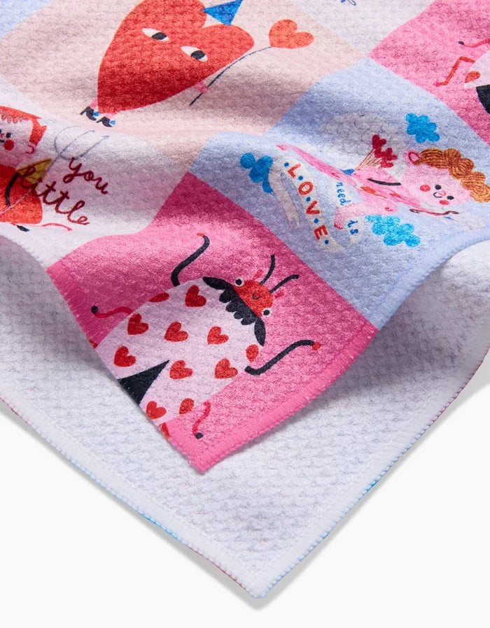 The Love Squares tea towel by Daria Solak is soft and colorful, with cartoon hearts, ladybugs, smiling faces, pastel pink, purple, blue squares, recycled materials, plus words like “love” and “You Little.”.