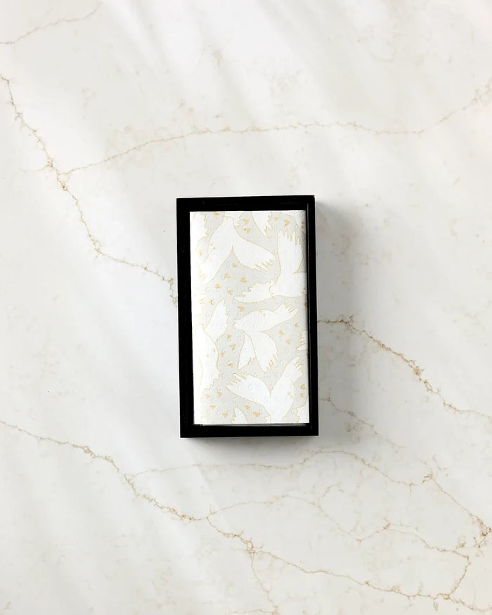 The GEOMETRY "Love Takes Flight" soap, a rectangular white bar with a gold bird pattern, is showcased in a black box on white marble with tan veining, enhancing eco-friendly kitchen towels for a sustainable vibe.