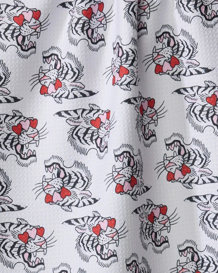 The Cole Strem Love Tiger tea towel features white fabric with a repeating cartoon tiger pattern—heart-shaped eyes, red noses, and snarling faces. Ultra-absorbent and made from recycled materials, it has a slightly dimpled texture.