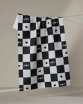 The GEOMETRY "Loving" tea towel features a black and white checkered pattern with MOM and heart symbols on some squares, hanging on a line against a neutral background.