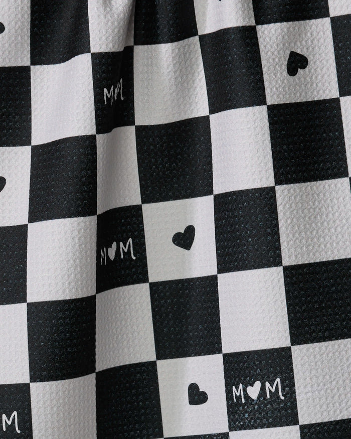 A close-up of the GEOMETRY Loving dish towel shows its black and white checkered, textured surface with black hearts and "M♥M" in some squares. Stylish and absorbent, it's perfect for functional kitchen use.