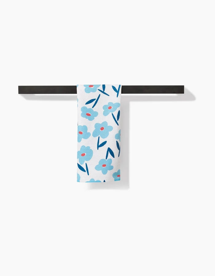 The Luca Daisy Bar Towel by Hufton Studio features blue flowers with pink centers and dark blue leaves on white Geoweave fabric, shown hanging neatly on a black towel bar against a white background.