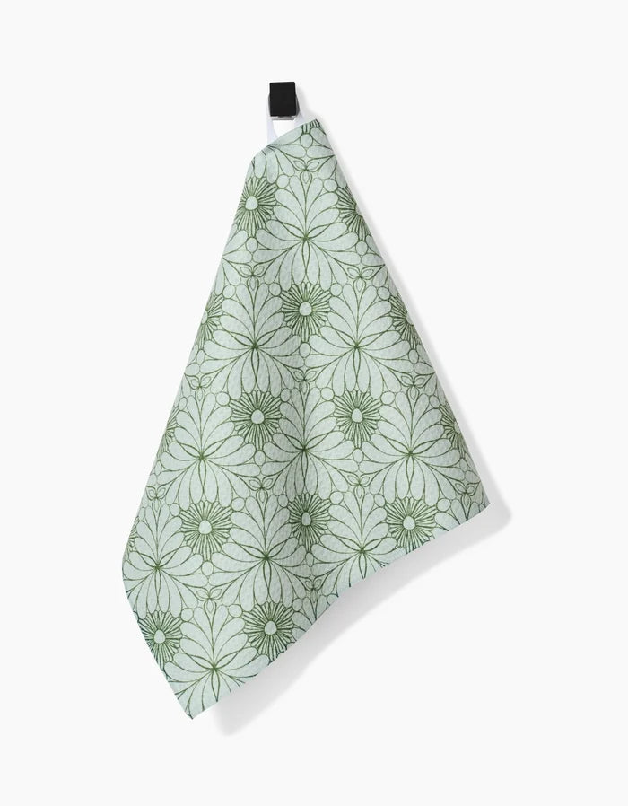 The Marta Harvey Lush Green Floral bar towel, made from ultra-absorbent Geoweave fabric, displays a symmetrical dark green floral pattern on light green and hangs by a black loop against a white background.