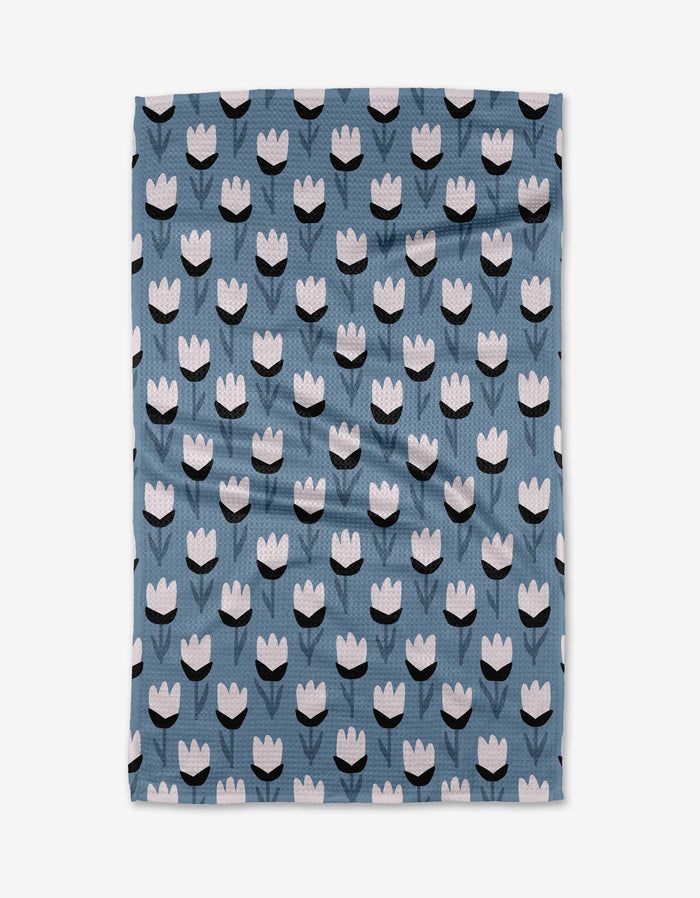 The Lush Meadow tea towel by Anette Heiberg features white and black tulip-like flowers in rows on blue Geoweave fabric—ultra-absorbent for both style and function.