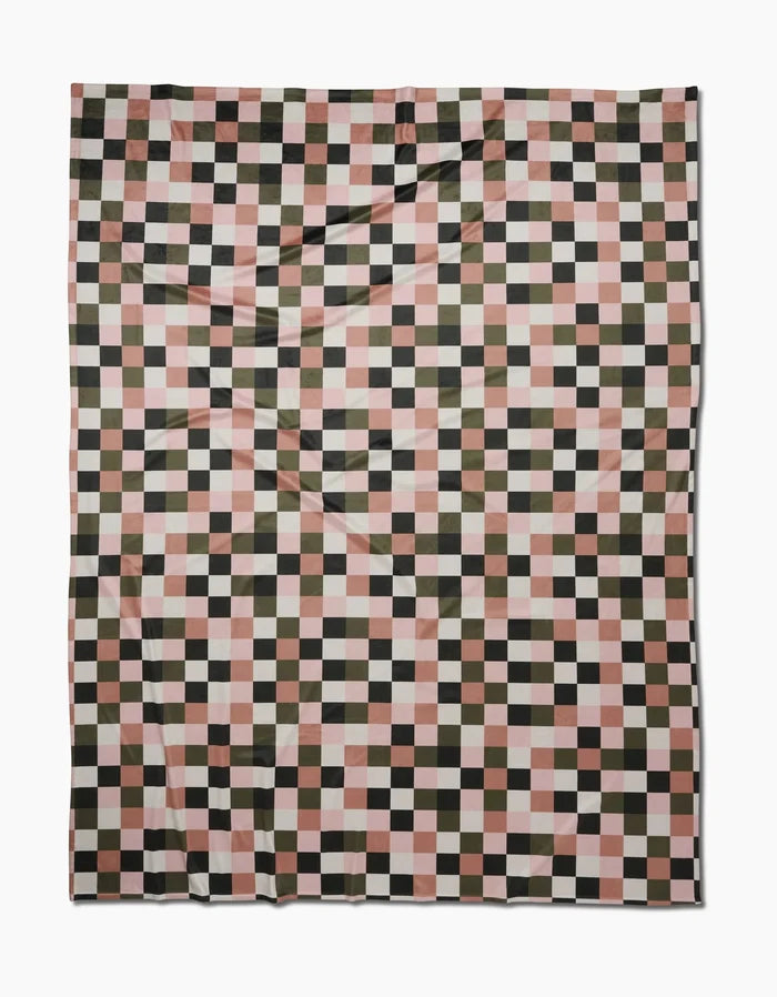 The Luxora by Geometry is an eco-friendly blanket with a checkered pattern in black, olive green, pink, and white squares, laid flat on a white background and made from recycled materials.