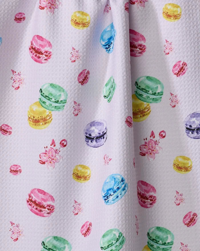 The "Macarons in Paris" tea towel by Travel Write Draw features a white textured design with colorful macarons and pink flowers, crafted from recycled materials for an eco-friendly kitchen accent.