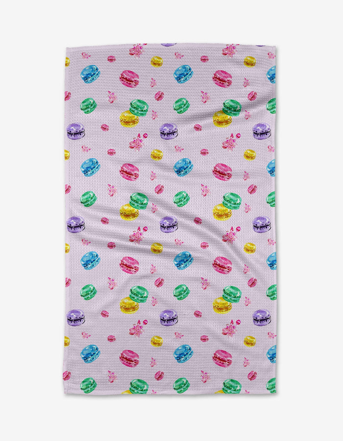The Macarons in Paris tea towel by Travel Write Draw features a white background adorned with colorful macarons—pink, yellow, green, blue, and purple—and playful pink bows.