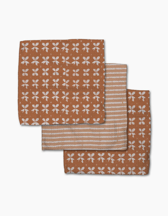 Three folded brown Maceta napkins by Geometry: two with a white floral pattern, one with white horizontal stripes. Made from recycled materials, they’re a sustainable addition to your dishcloth collection.