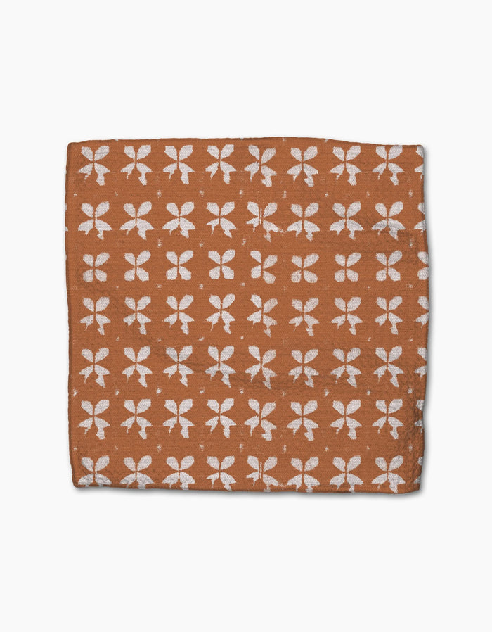 The Geometry Maceta is a square brown dishcloth made from recycled materials, featuring a repeated white floral pattern and displayed flat against a white background.