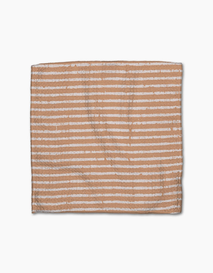 The Geometry Maceta is a rectangular light brown dishcloth made from recycled materials, featuring evenly spaced uneven horizontal white stripes, displayed on a white background.