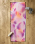 The GEOMETRY Magenta yoga mat, featuring pink, orange, and purple swirls, rests on a wooden floor. A white water bottle sits at the bottom left corner with two gray yoga blocks and a non-slip towel at the top right.