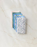 Six Magic Field reusable paper towels by Happy Hemera in pastel blue, green, lavender, and pink are neatly stacked on a white marble surface with subtle brown veining.