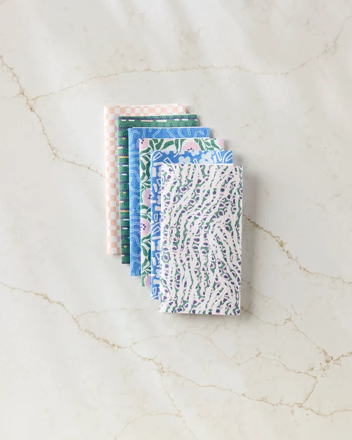Six Magic Field reusable paper towels by Happy Hemera in pastel blue, green, lavender, and pink are neatly stacked on a white marble surface with subtle brown veining.