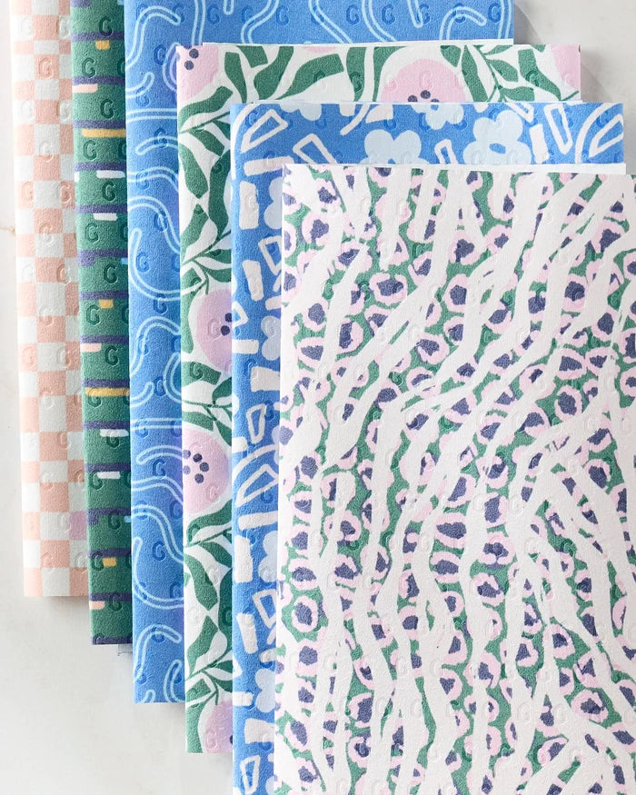 Six Magic Field cleaning cloths by Happy Hemera, featuring checkered, swirl, floral, and abstract animal patterns, are fanned out on a light surface—an eco-friendly alternative to reusable paper towels.