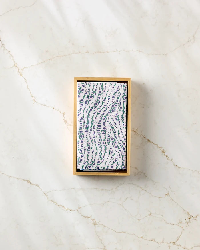 A rectangular box of Magic Field eco-friendly paper towels by Happy Hemera, with a white lid and blue-green abstract pattern, sits on a subtly veined light marble surface.