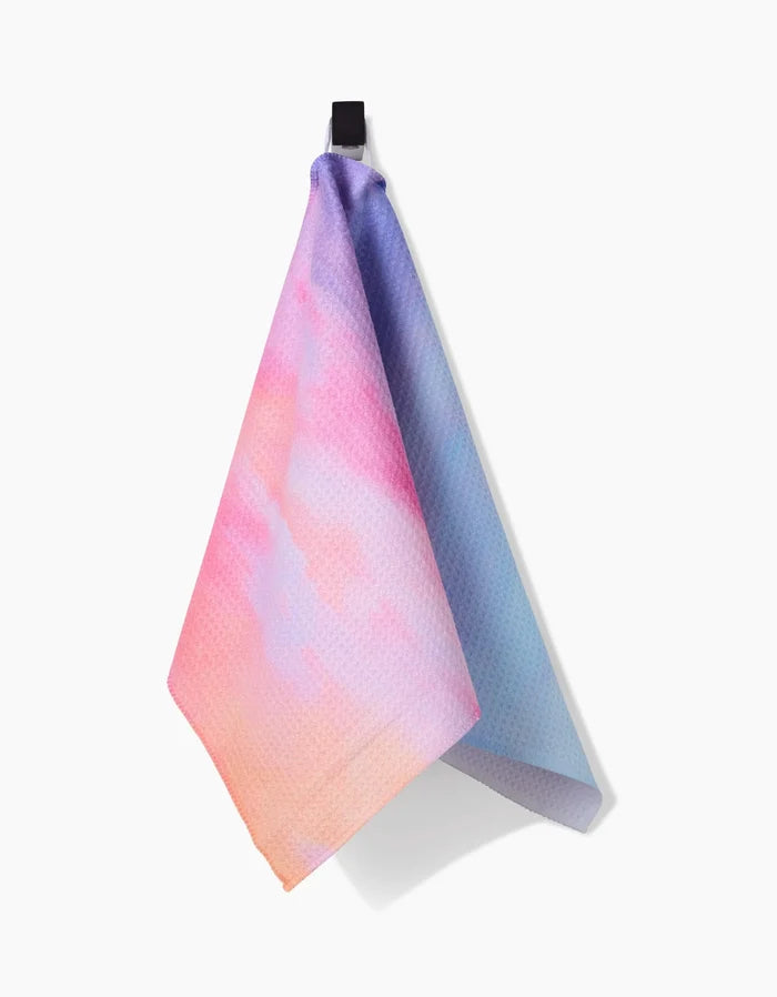 The Magic In The Sky Bar Towel by Stefanie Bales, crafted with Geoweave™ fabric for superior absorbency, displays a vibrant gradient of pink, purple, blue, and orange and hangs from a black hook against a white background.